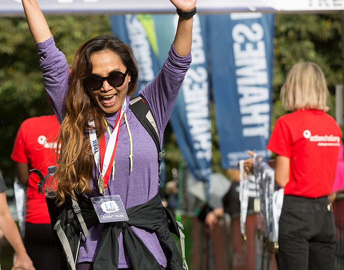 A woman raises her arms in triumph as she crosses the finish line of a the Thames Bridges Trek.
