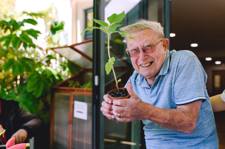 A smiling patient holding a small plant - at the Living Well group.