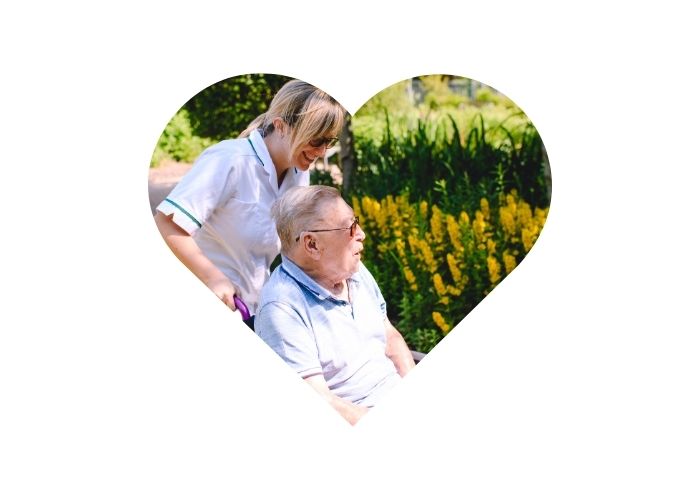 A patient in a wheelchair with an occupational therapist - taking a walk around a garden. Encased in a love heart.