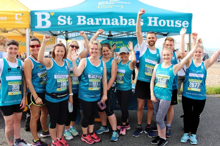 a group of runners in St Barnabas House vests standing by a St Barnabas House branded gazebo