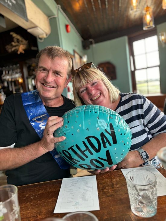 A man and a woman sit in a pub or restaurant with blue balloon that says 'Birthday Boy'