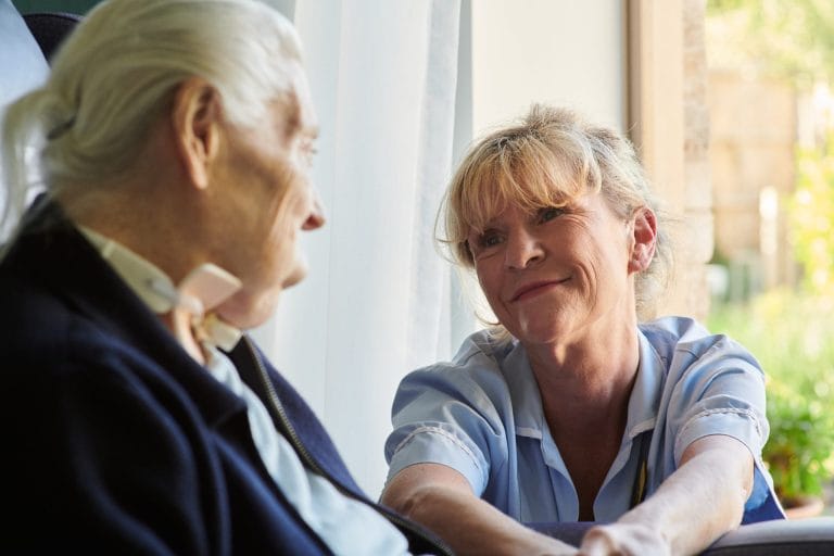 A clinical member of staff sits with a hospice patient smiling at her.