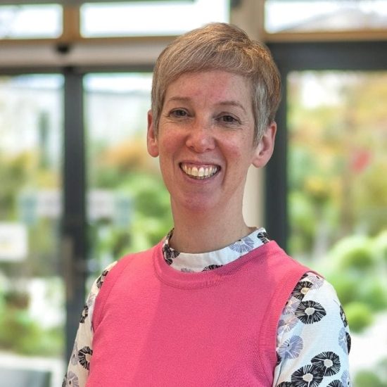 A woman stands smiling against the background of a hospice interior which is brightly lit
