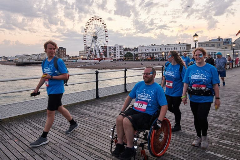 A group on Worthing pier taking part in night to remember. A teenager, man in a wheelchair and two women make their way along the pier