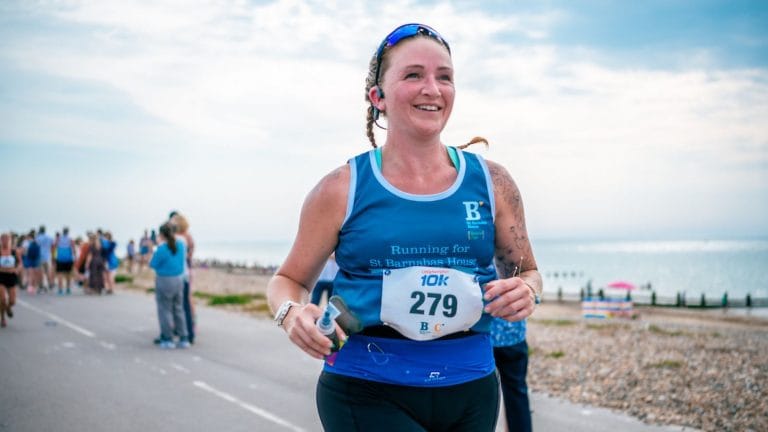 Runner at a seafront running event, smiling and wearing a St Barnabas House running vest