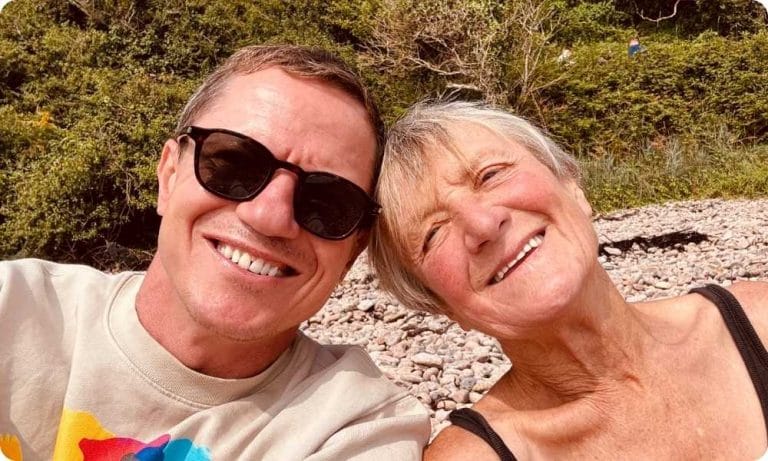 Matt and his mum pose with big smiles and the heads together. Matt is wearing sunglasses.