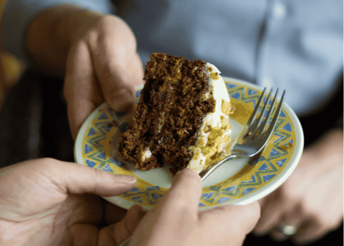 Two hands hold a small plate with cake on it