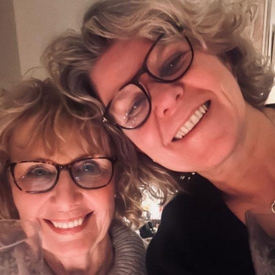 A mother and daughter in a selfie, both smiling and holding a wine glass.