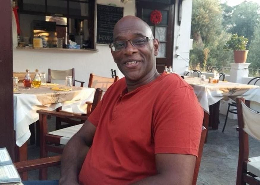 Derrick sitting at a table outside a restaurant, smiling at the camera