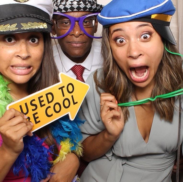 Derrick and his daughters in a photobooth, wearing and holding props and pulling faces