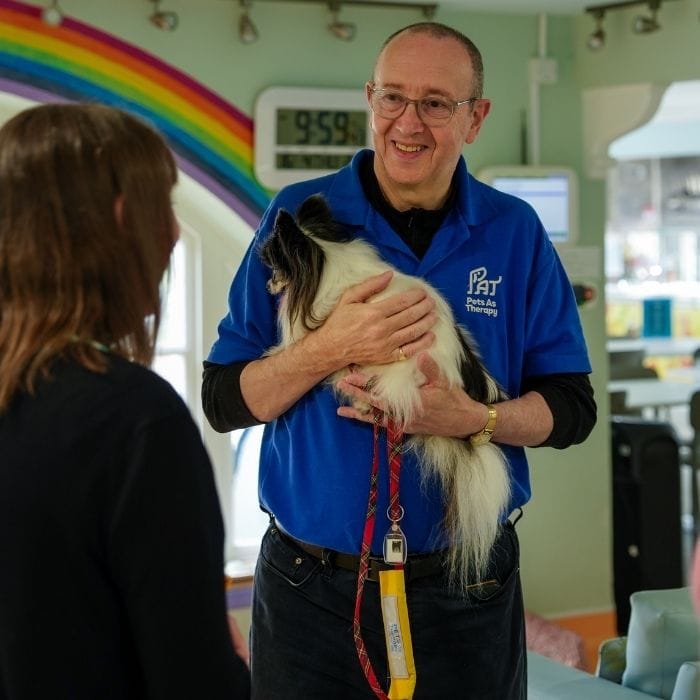 A man stands holding a small dog while speaking to another person