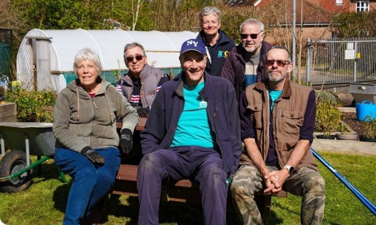 A group of people sits outside in a garden smiling at the camera