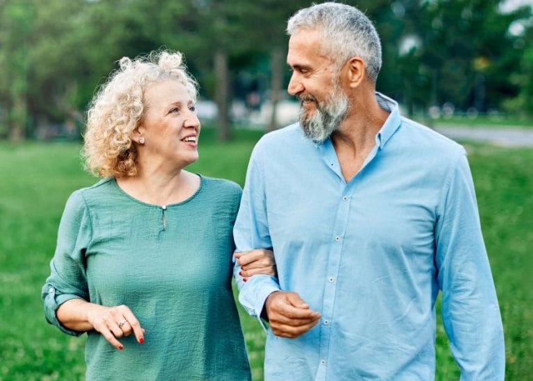 Man and woman walking arm in arm outdoors. They are looking at each other and smiling