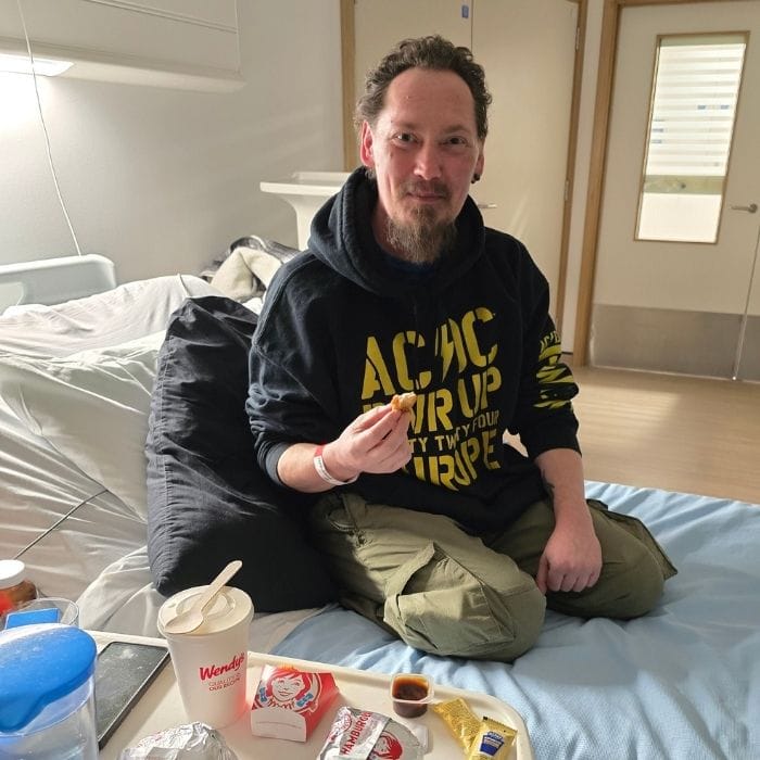 Carl sitting on a hospital bed eating takeaway