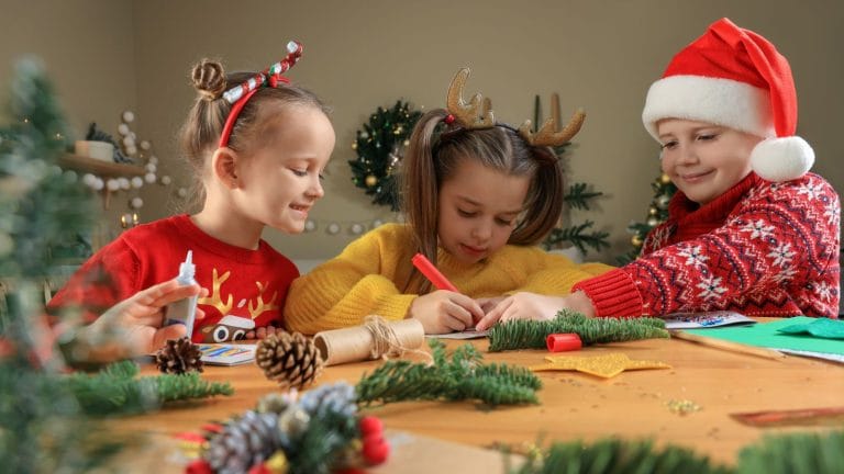 three children sitting at a tabl with festive jumpers and accessories taking part in festive crafts